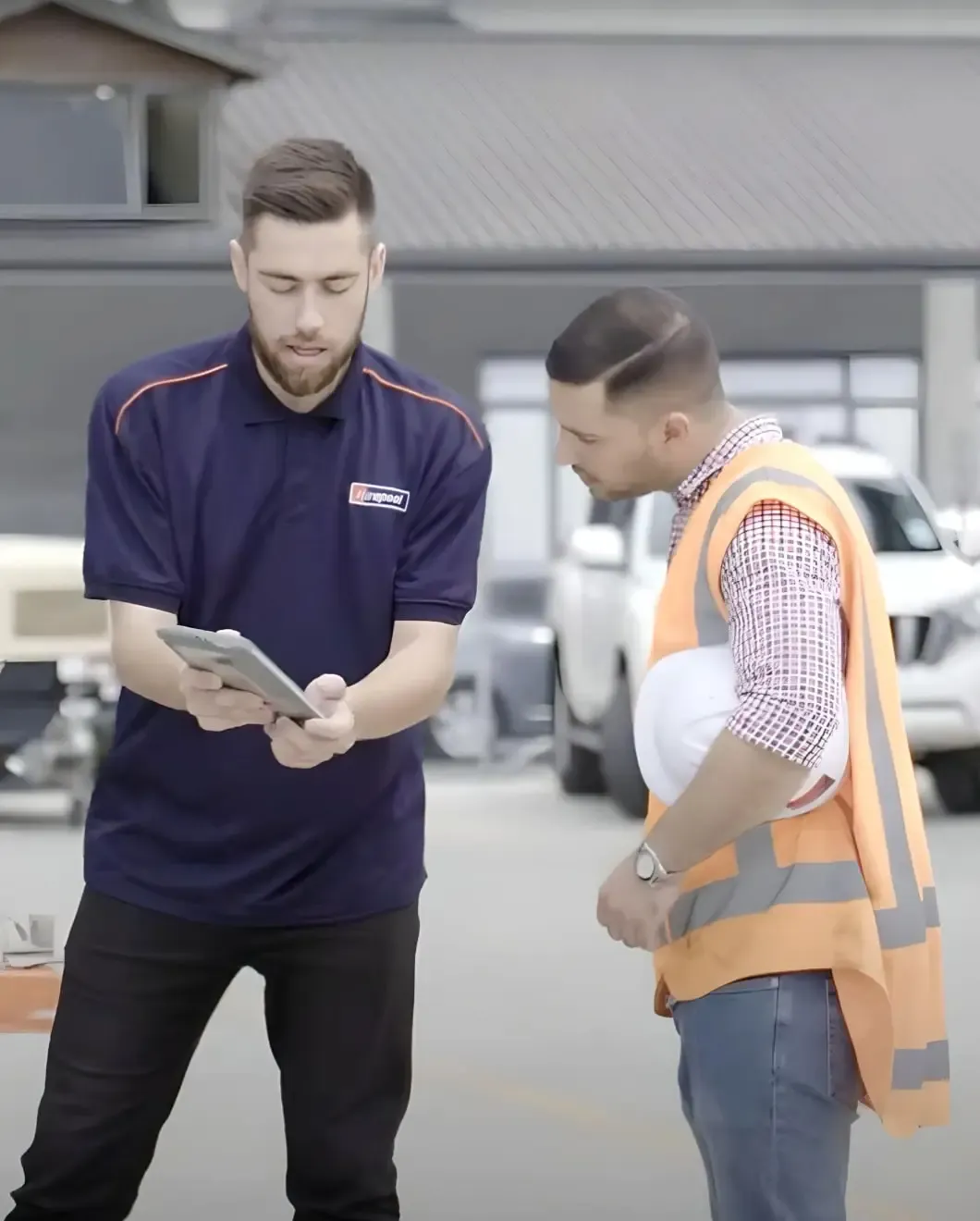 Hirepool staff member showing the hire platform on a tablet to a customer in a hi-vis vest in the yard