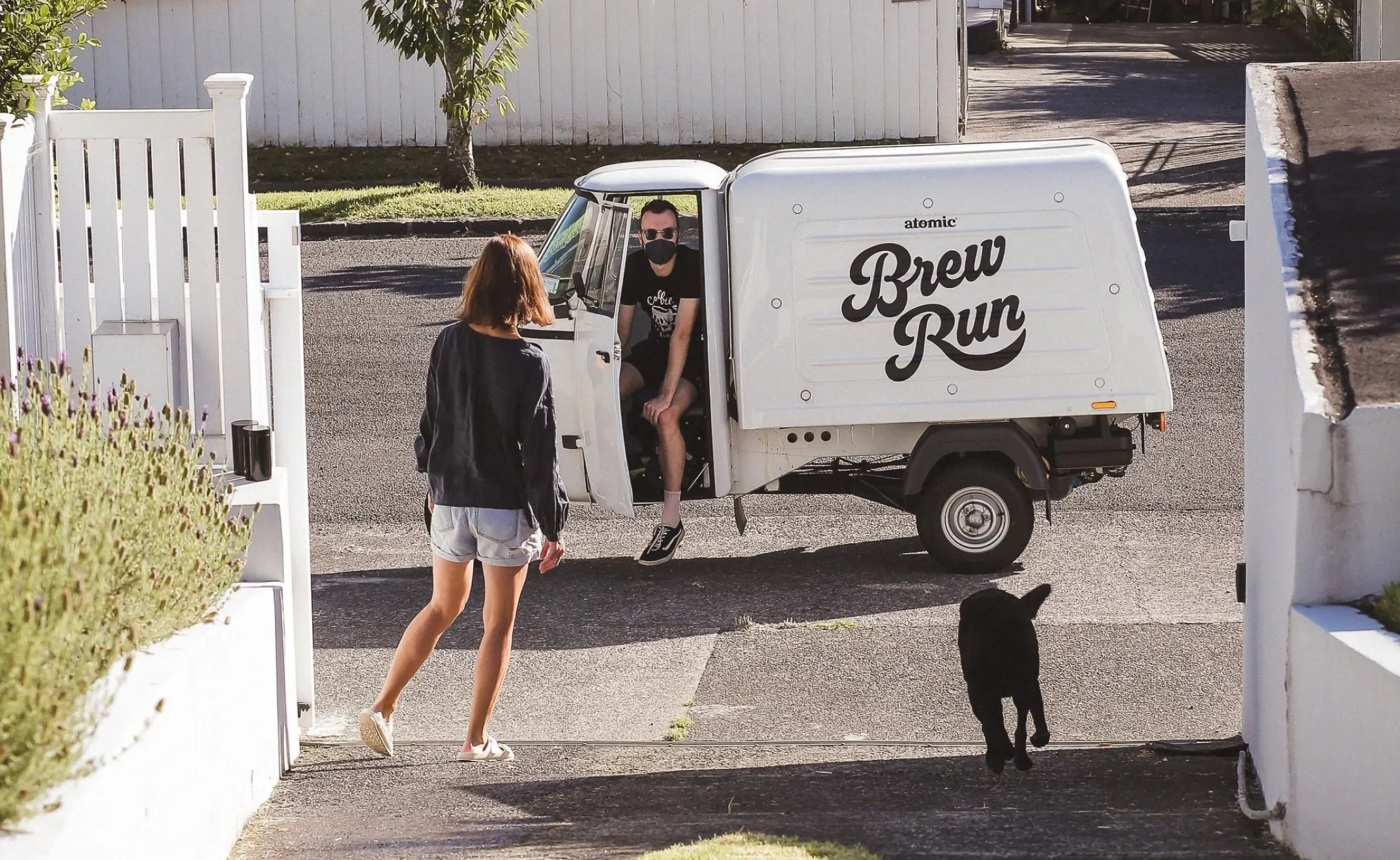 Atomic Brew Run driver in the branded delivery van greeting a customer at the gate