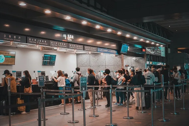 A large crowd of people lined up between barriers at indoor ticket counters, the kind of physical queue congestion virtual queuing removes