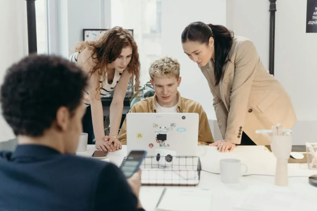 Three colleagues gathered around a laptop in an office reviewing software together
