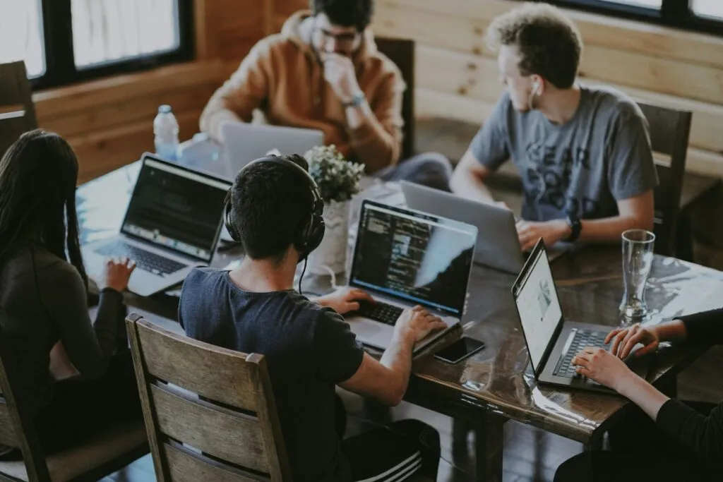 A team of developers coding on laptops around a shared table, building custom software together